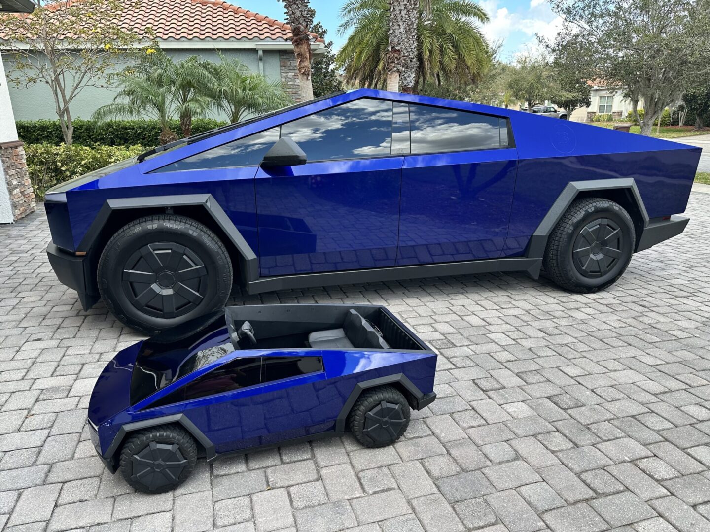 A blue Tesla Cybertruck with a matching small toy model parked on a driveway.