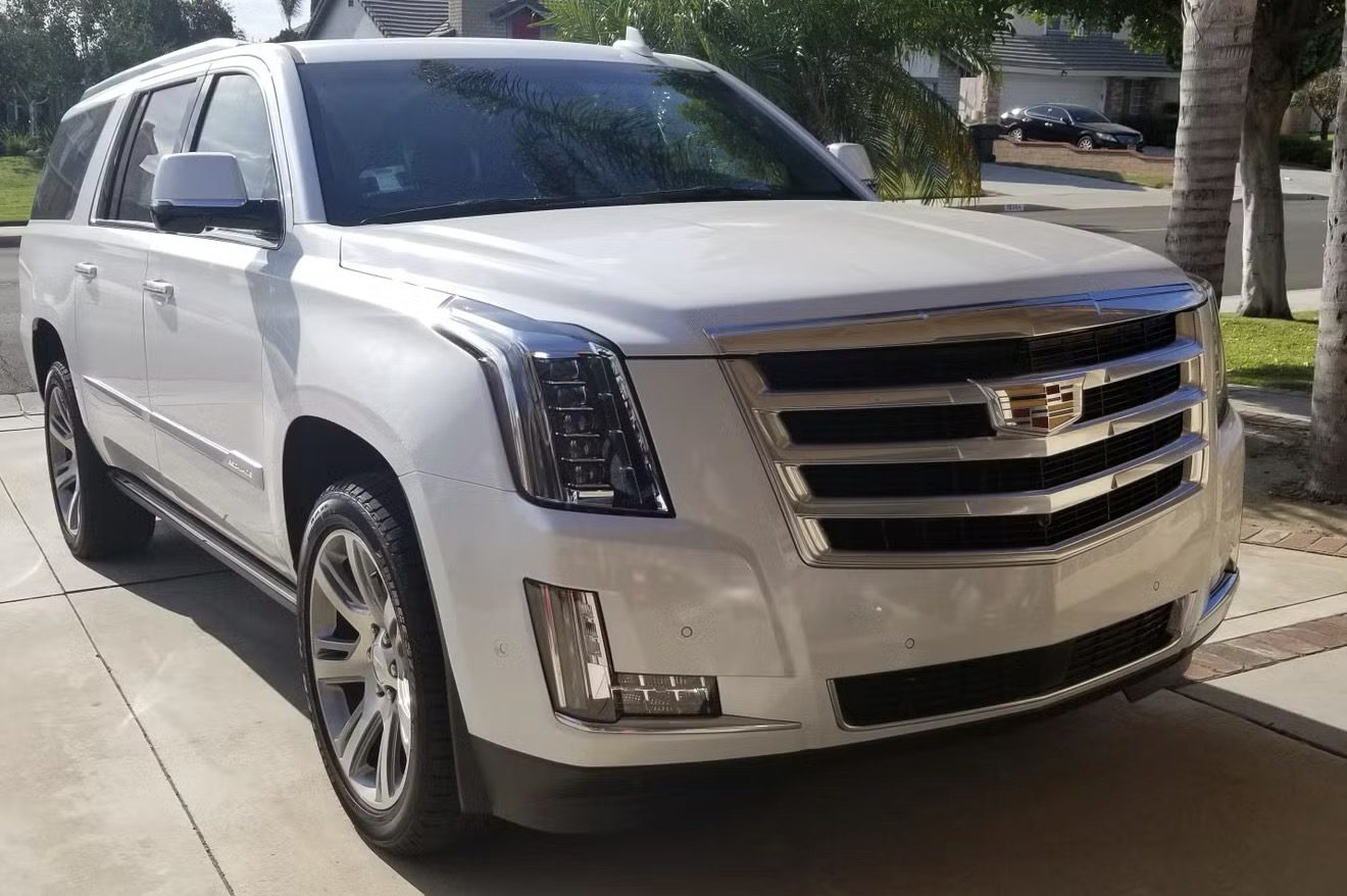 White Cadillac SUV parked near trees on a sunny day.