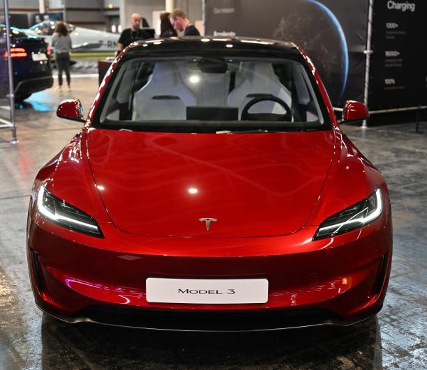 A shiny red Tesla Model 3 parked indoors.